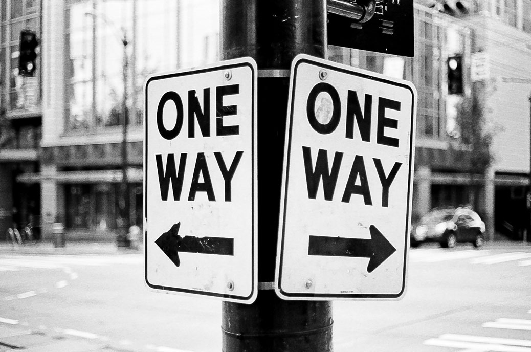 Street scene with two road signs saying "one way" pointing in different directions